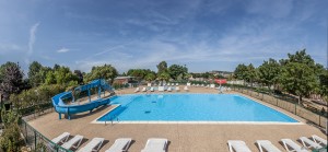 Cette photographie représente une piscine extérieure avec un toboggan et des chaises longues disposées tout autour.