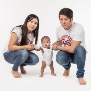 Photographie d'un couple avec leur enfant qu'ils font tenir debout.