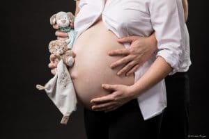 Photographie d'une femme enceinte avec les futur doudous de son enfant.